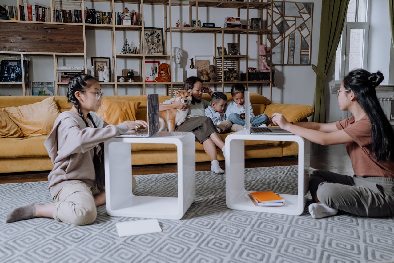 Asian family enjoying leisure time together at home with laptops and a dog in the living room.