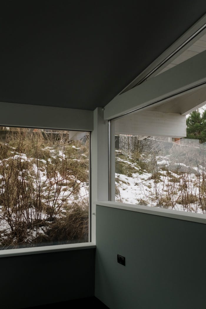 Minimalist interior with large windows overlooking a snowy outdoor scene, showcasing modern architecture.
